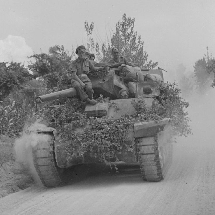 A Canadian M10 in Italy, driving along a
          dusty road. It has a lot of vegetation attached to it to try to
          camouflage it.