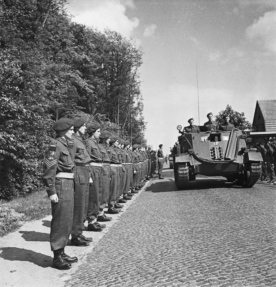 Several Archers drive down a road
          towards the camera, with soldiers standing to attention on either side
          of the road.
